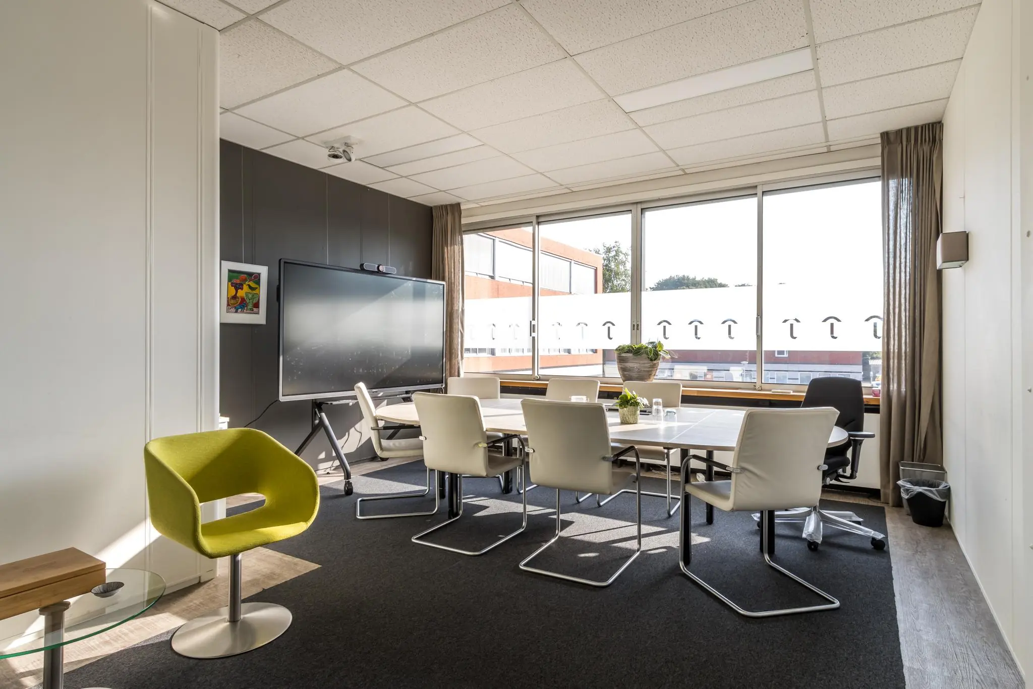 Vergaderruimte aan de Jan van Eycklaan met moderne inrichting, groot scherm en veel natuurlijk licht.